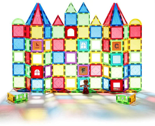 Structure colorée et complexe de château construite avec des jeux de construction magnétiques, comprenant des blocs transparents de différentes formes et couleurs, avec des caractères alphabétiques et une petite figurine de personnage posée devant.